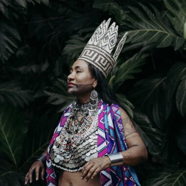 A woman in vibrant traditional Panamanian attire and crown poses against lush foliage.