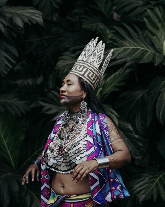 A woman in vibrant traditional Panamanian attire and crown poses against lush foliage.