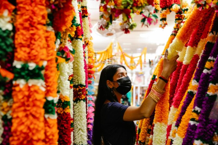 A woman wearing a mask shops for vibrant handmade floral garlands indoors.