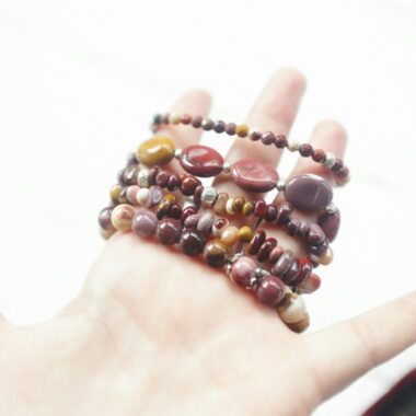 Close-up of a hand holding colorful beaded bracelets against a white background, showcasing vibrant jewelry.