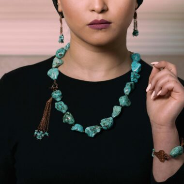 Close-up of a woman wearing turquoise necklace, earrings, and bracelet against a black outfit.