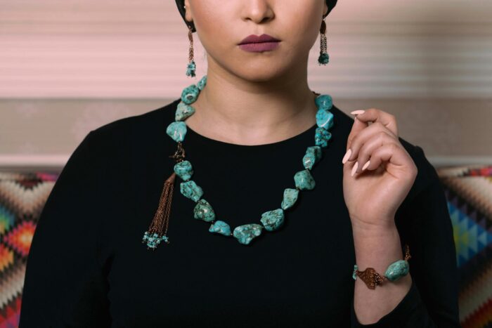 Close-up of a woman wearing turquoise necklace, earrings, and bracelet against a black outfit.